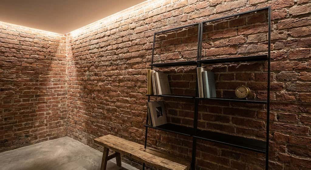 Detalle de iluminación LED rasante desde el techo que resalta la textura rugosa y las sombras de una pared de ladrillo visto antiguo.